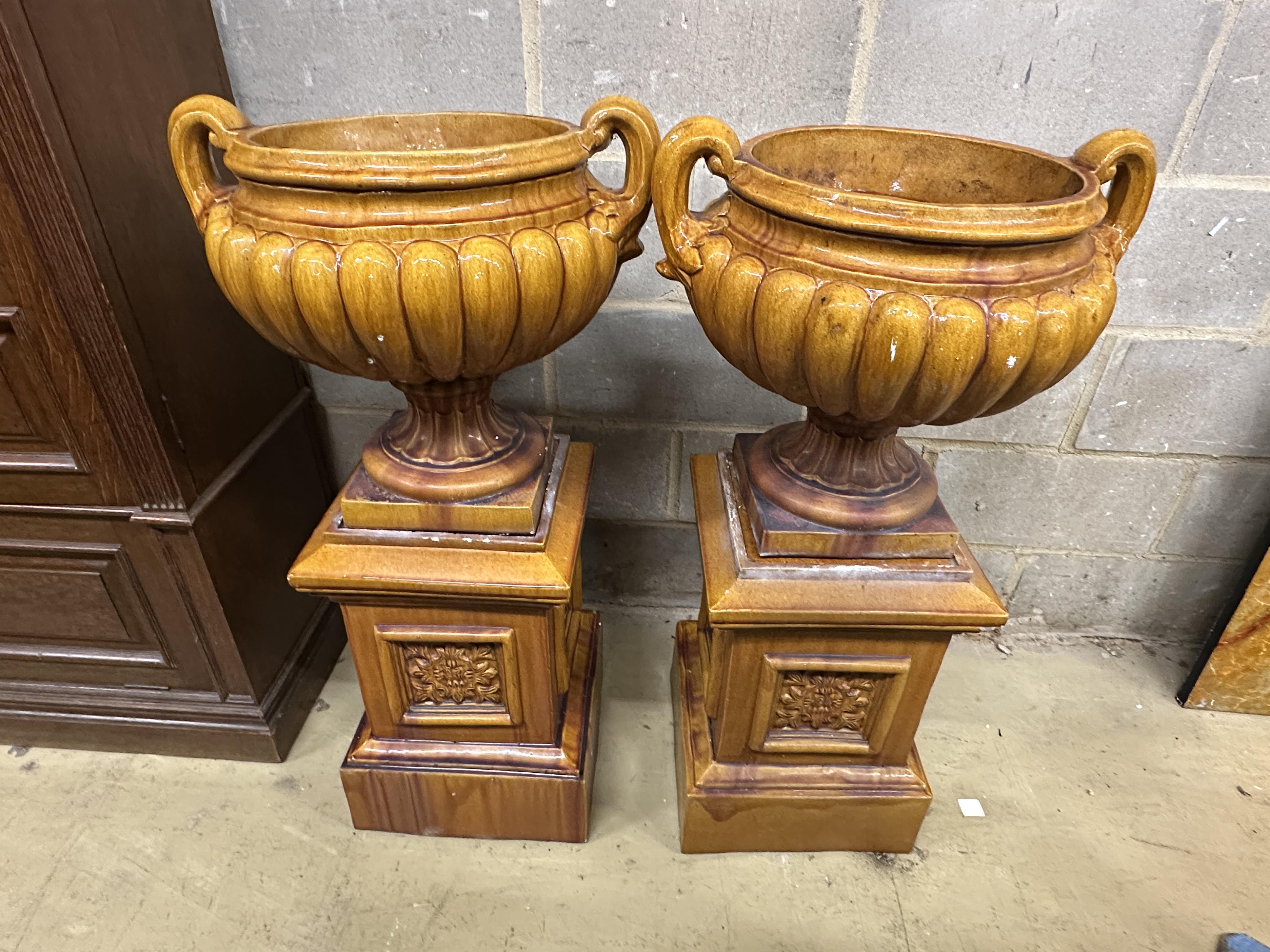 A pair of Victorian treacle glazed earthenware twin handled urns on square stands, height 104cm. Condition - fair, some losses to plinths